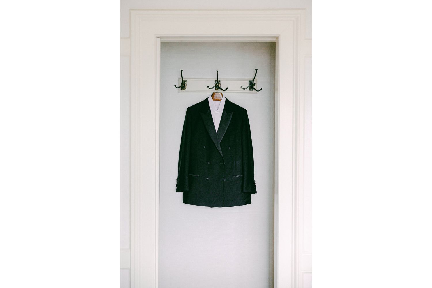 Dark green velvet blazer hanging on hooks against a white wall.