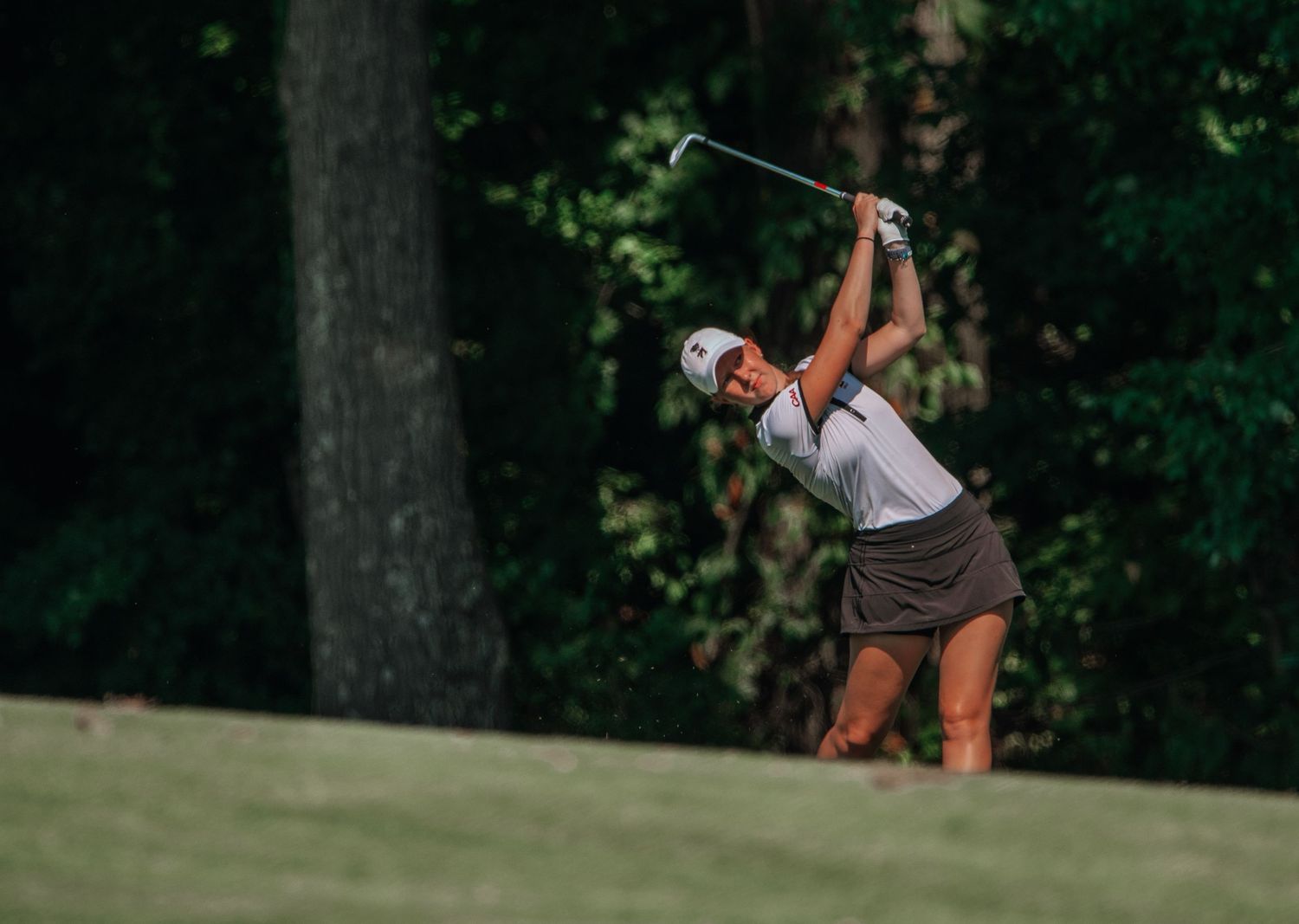 A golfer in athletic wear takes a powerful swing on a lush green course.