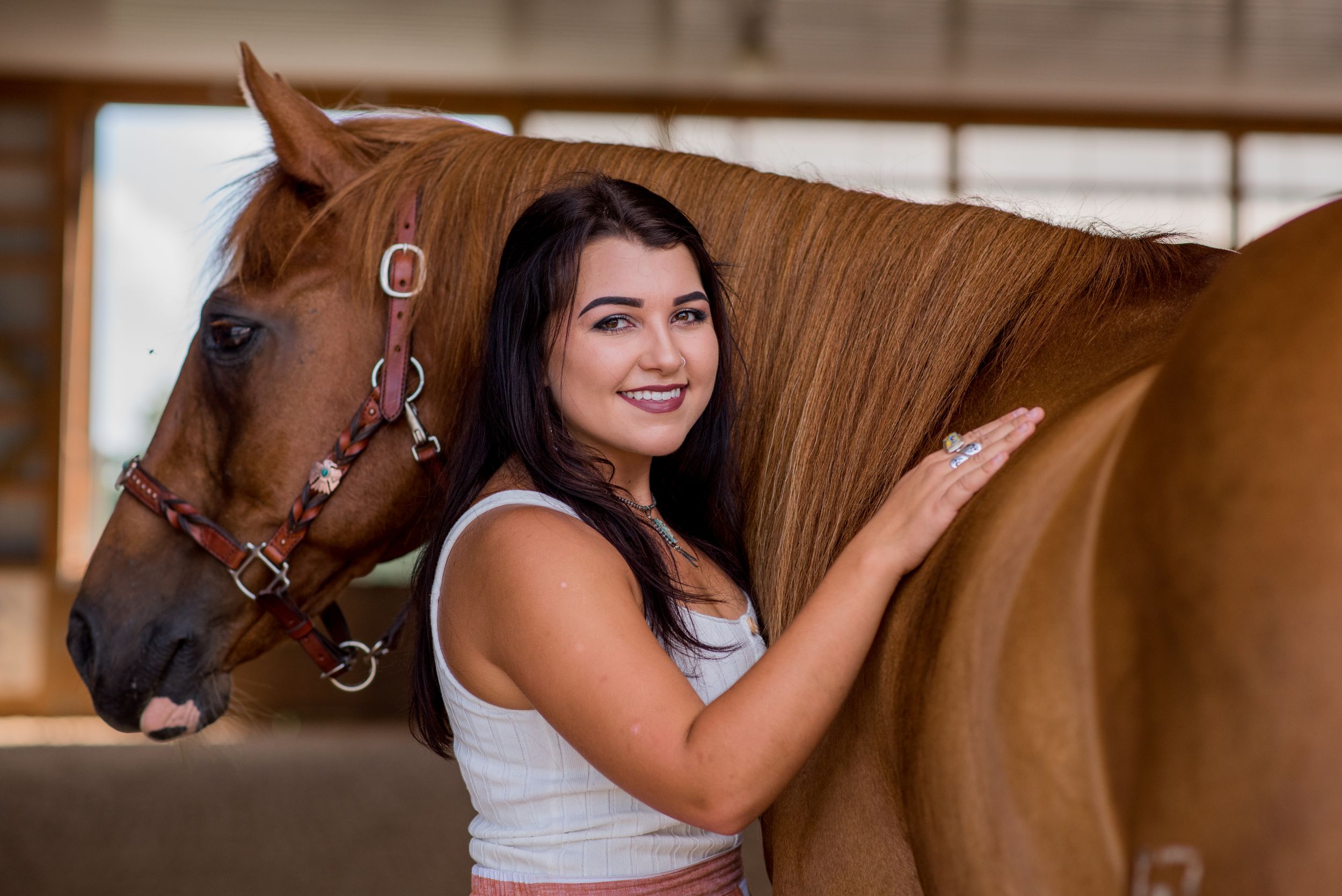 Brown horse with bridle stands close while being pet in stable setting.