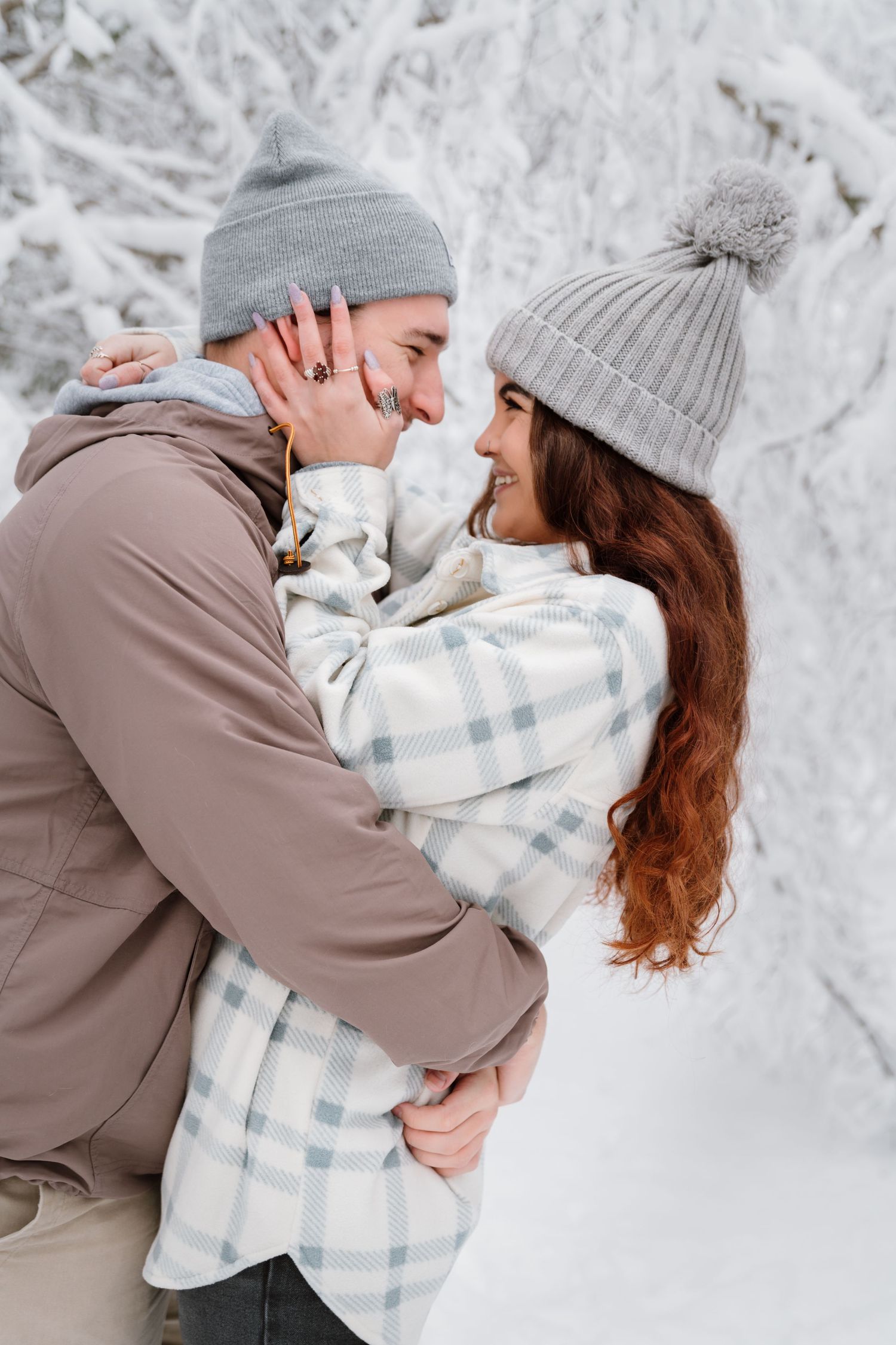 Intimate winter portrait of couple in matching gray beanies against snowy background.