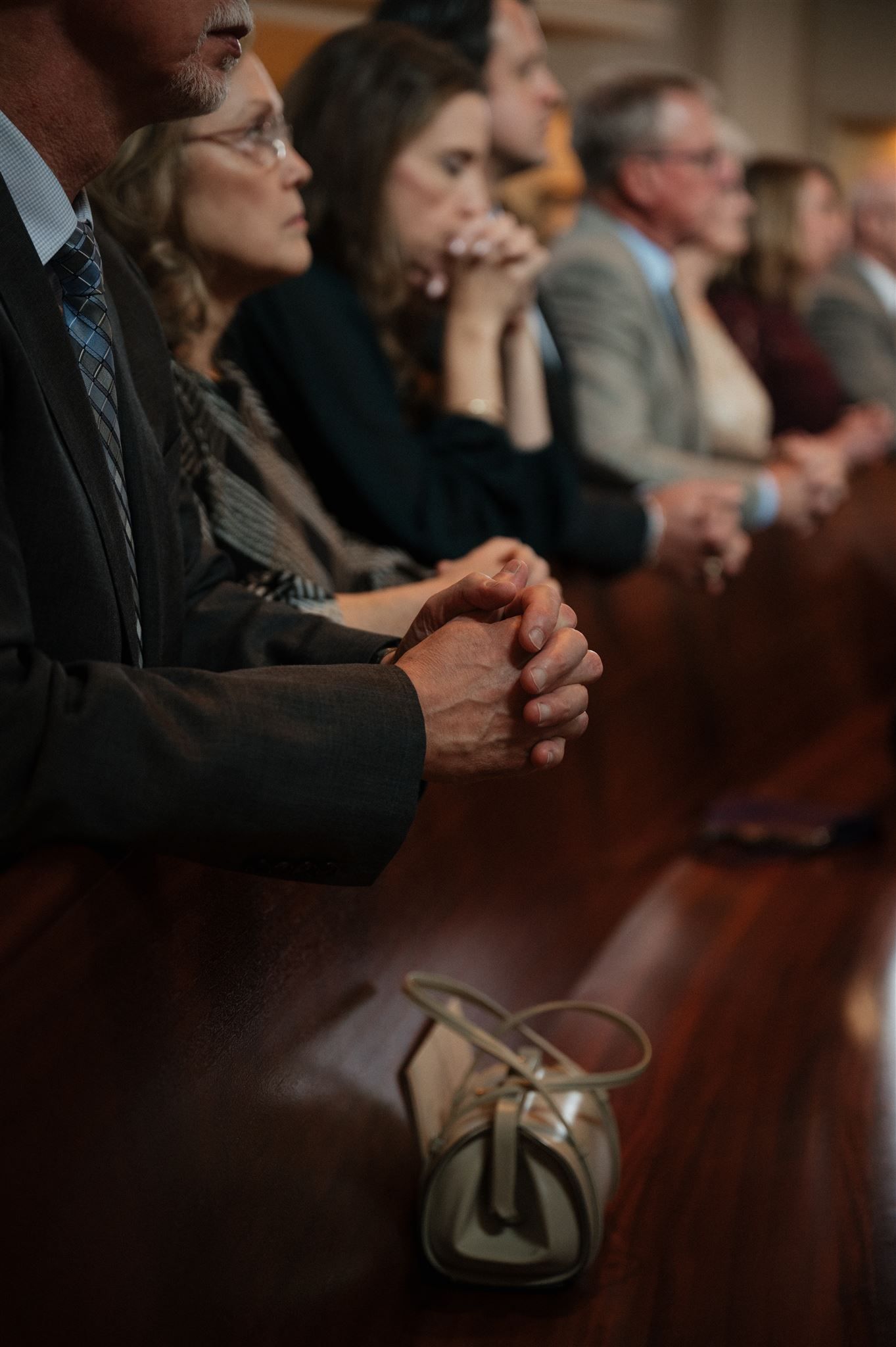 People sitting in church pews with clasped hands during a religious service.