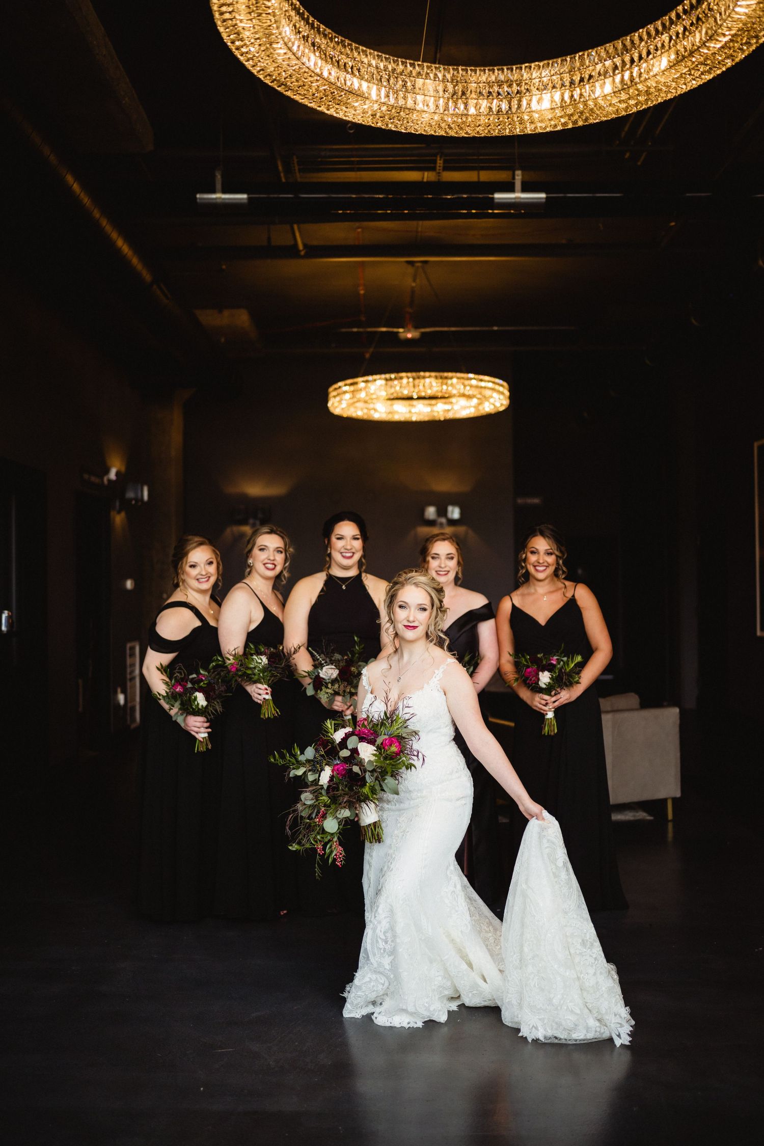 Wedding party poses dramatically under golden chandeliers in an elegant dark venue.