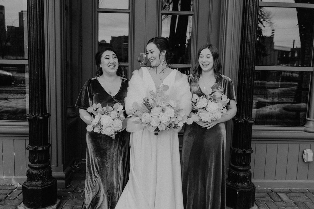 Black and white photo of bride and two bridesmaids laughing together holding floral bouquets.