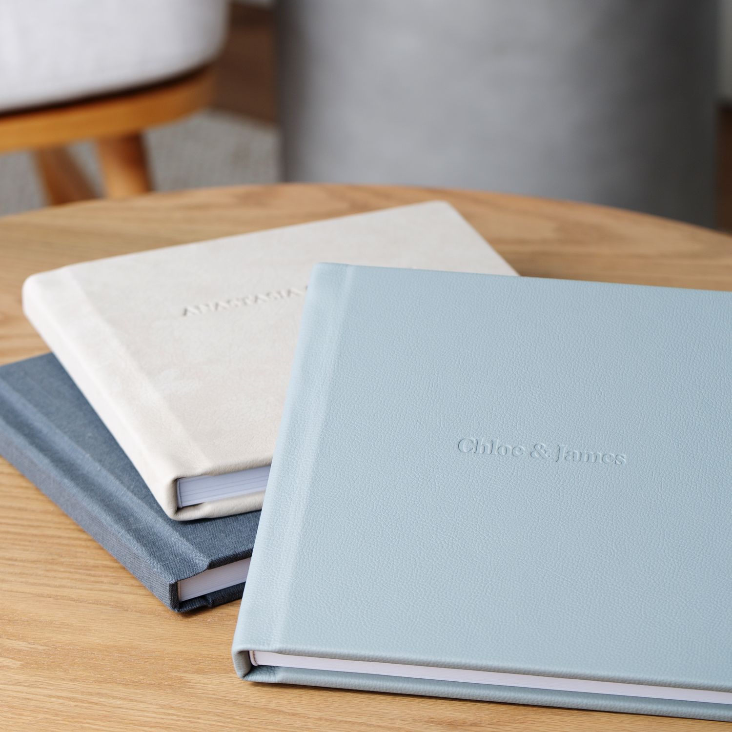 Three elegant photo albums in light blue and gray colors arranged on a wooden table surface.