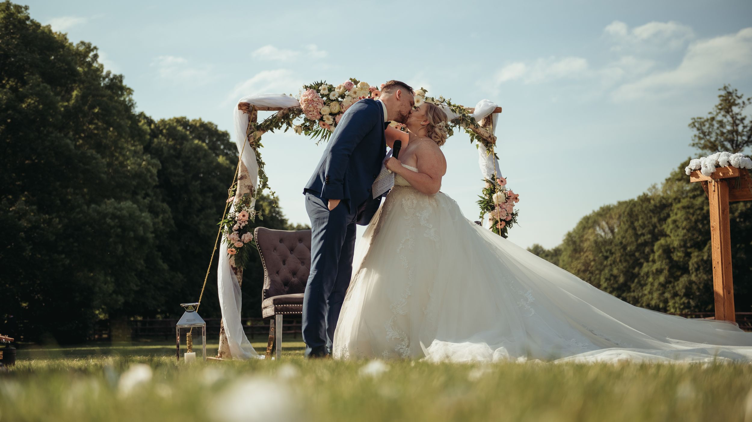 Bride and groom sharing a kiss under a floral arch at an outdoor wedding ceremony.