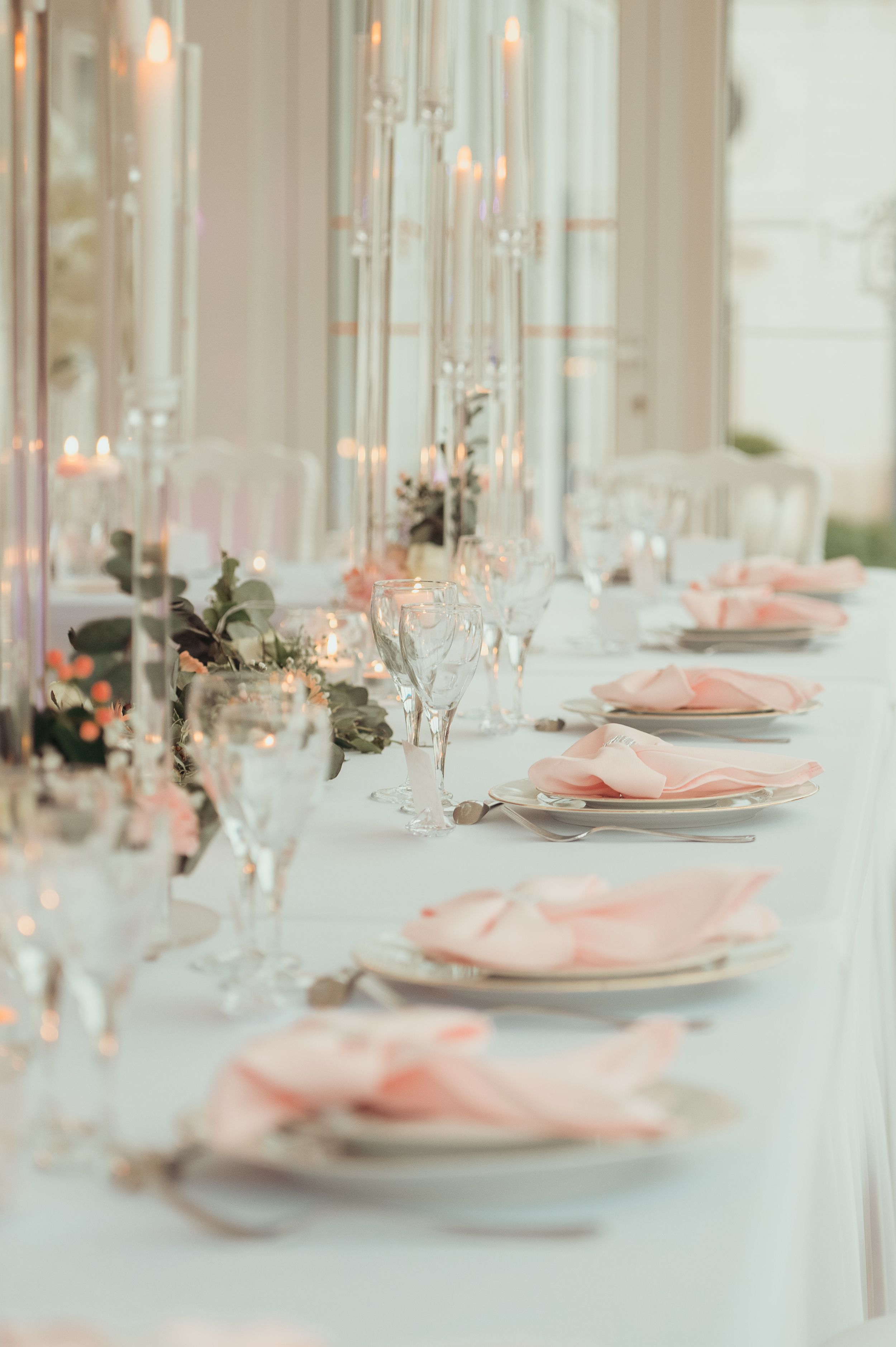 Sophisticated wedding reception table with pink linen napkins, crystal glassware, and tall candelabras in soft light.