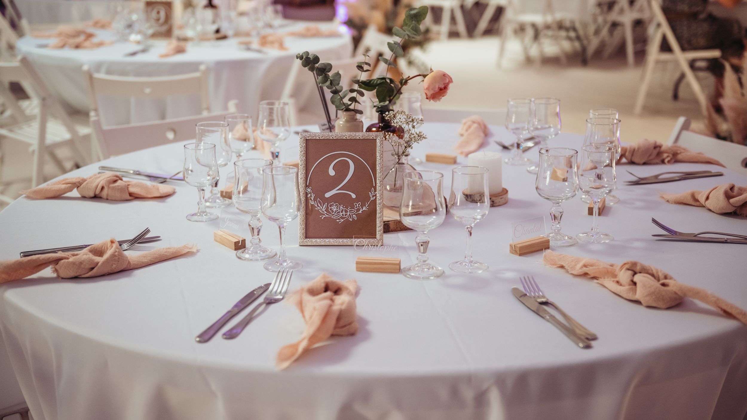Elegant wedding reception table set with pink napkins, crystal glasses, and a floral centerpiece numbered two.
