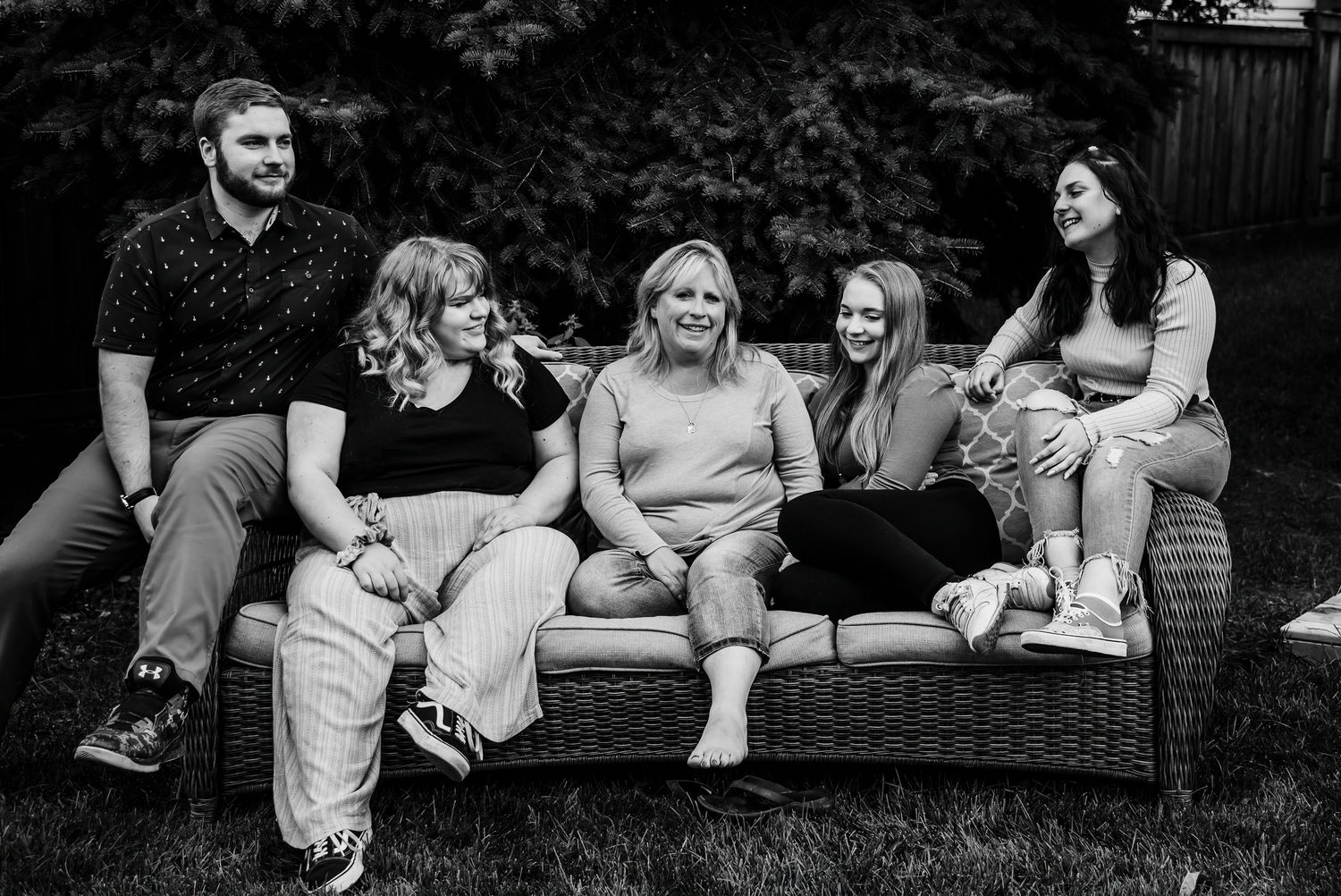 Group relaxing together on outdoor patio couch during casual gathering in backyard garden.