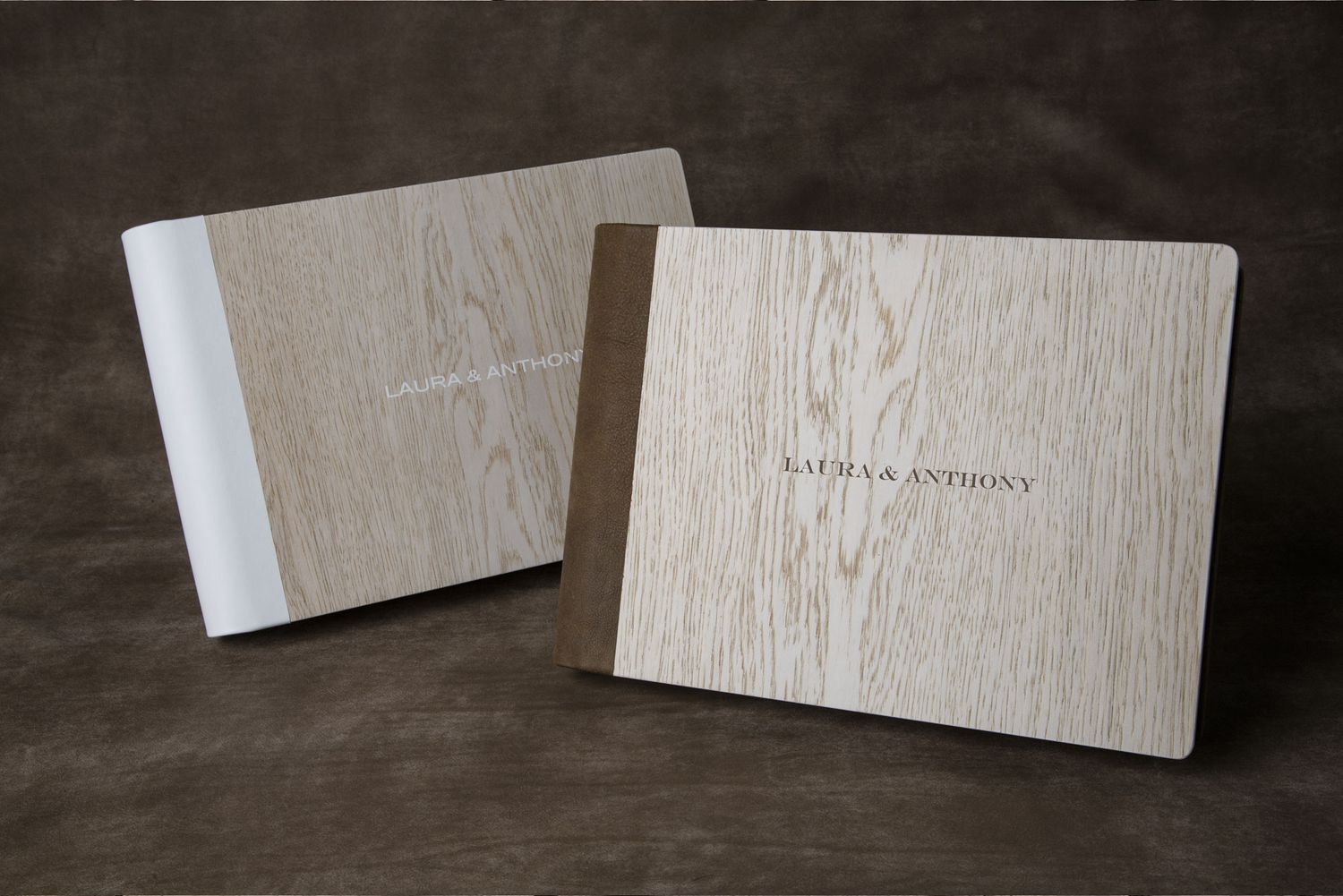 Professional wedding photo albums with light wood texture covers displayed on dark surface.