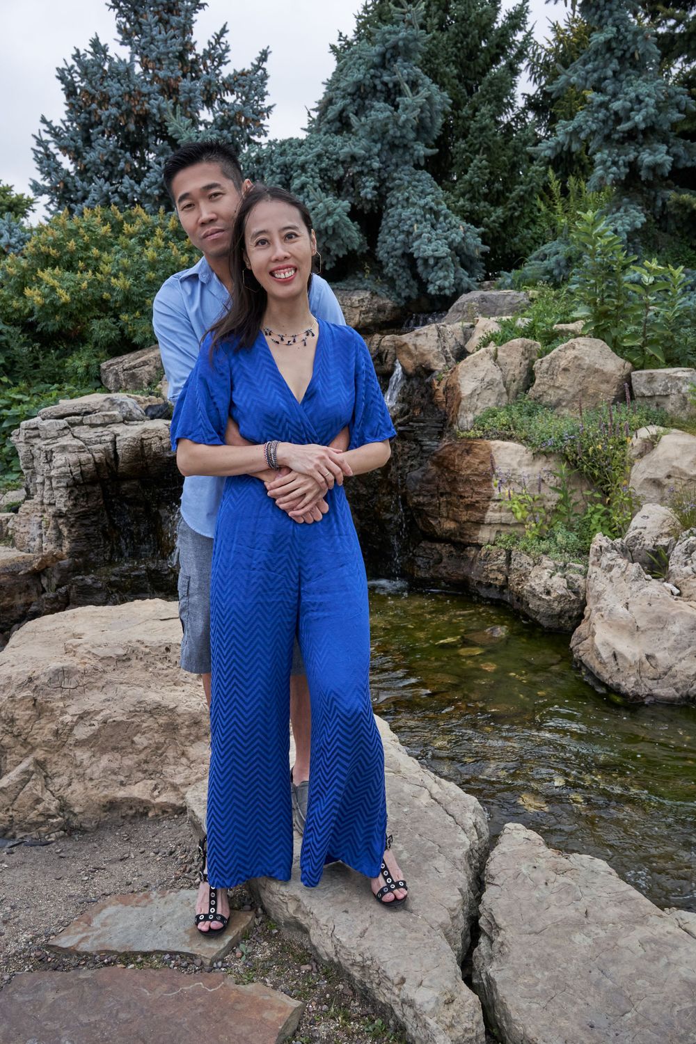 Couple posing together on rocky landscape with blue spruce trees in background.