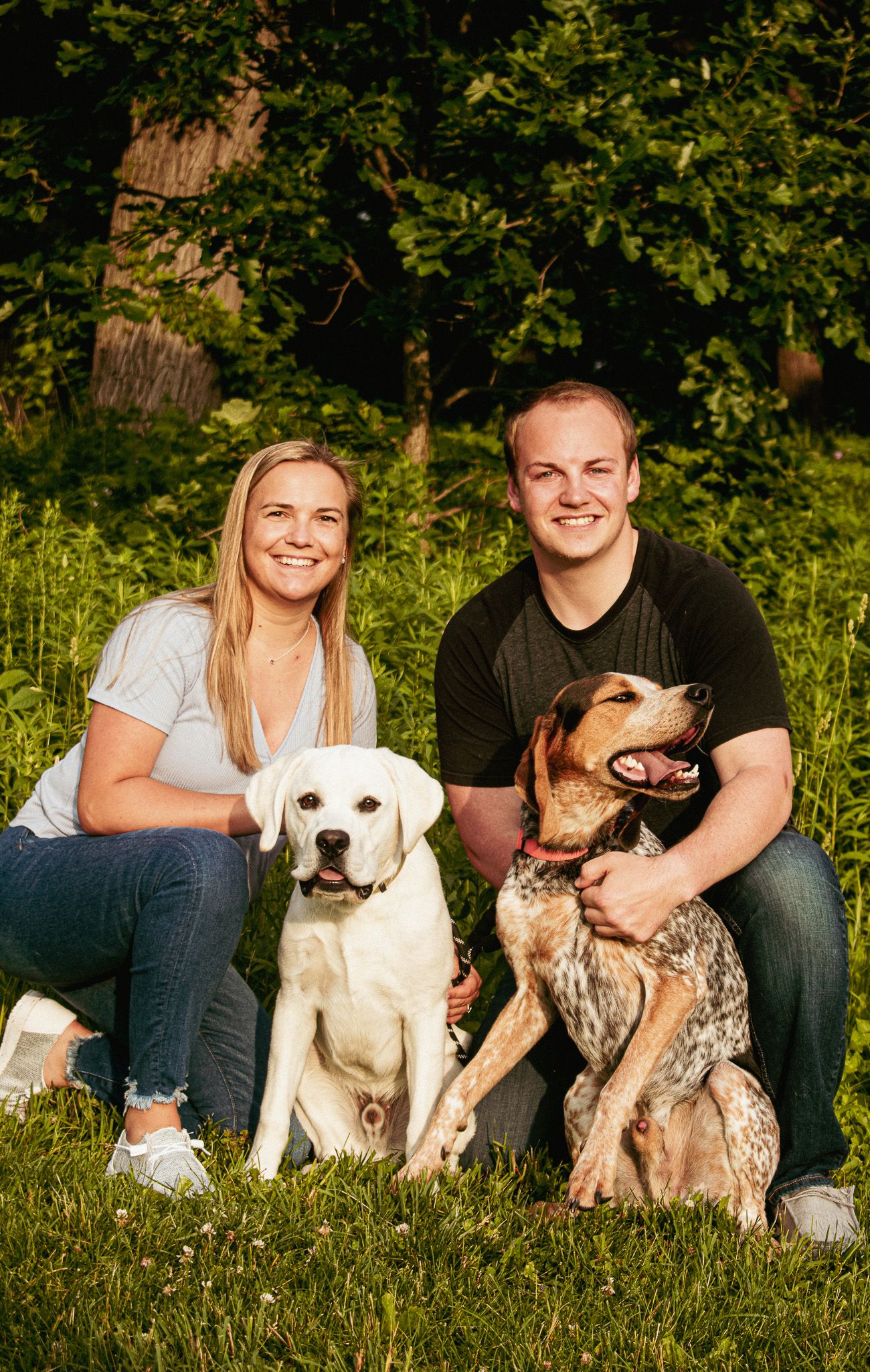A couple sitting outdoors with their two dogs, a white Lab and a brown mixed breed.