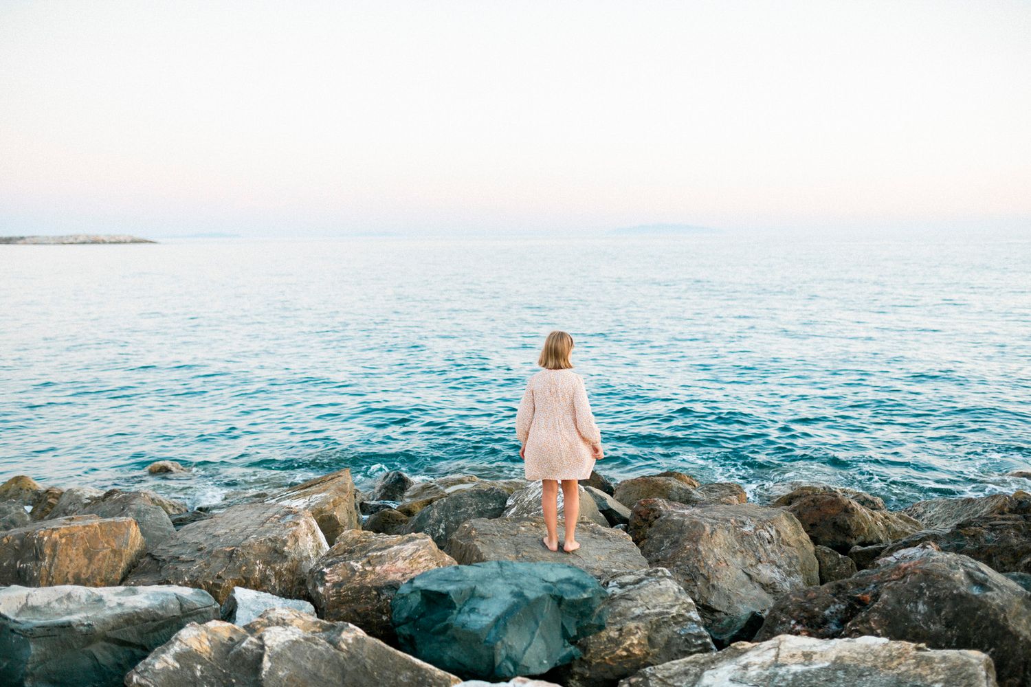 Person standing on rocky coastal outcrop overlooking the ocean at dusk.