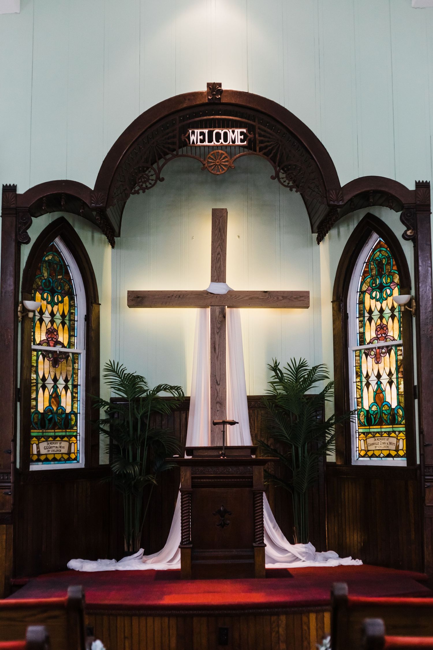 Church sanctuary with wooden pews, stained glass windows, and large wooden cross.