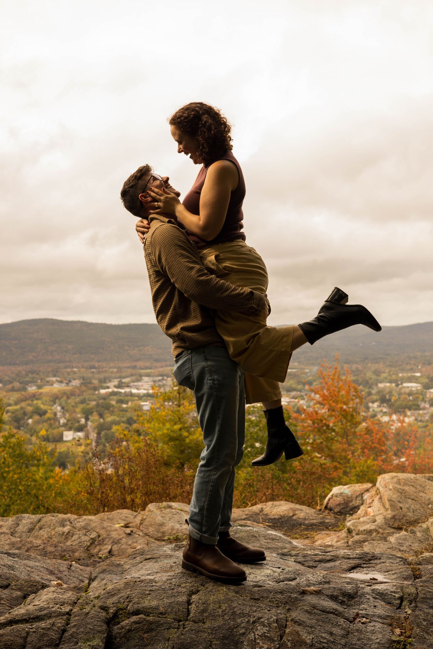 Romantic couple sharing intimate moment on rocky overlook during autumn sunset.