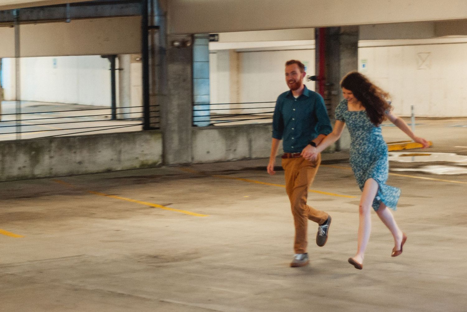Couple holding hands and running in a parking garage in Greenville, South Carolina