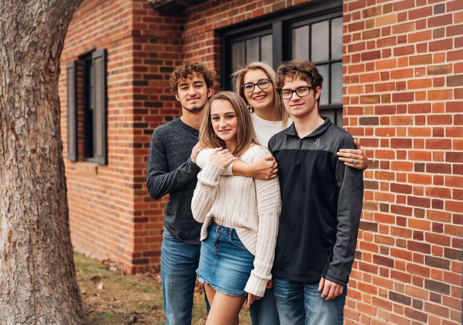 Family members pose together against a brick building exterior on a sunny day.