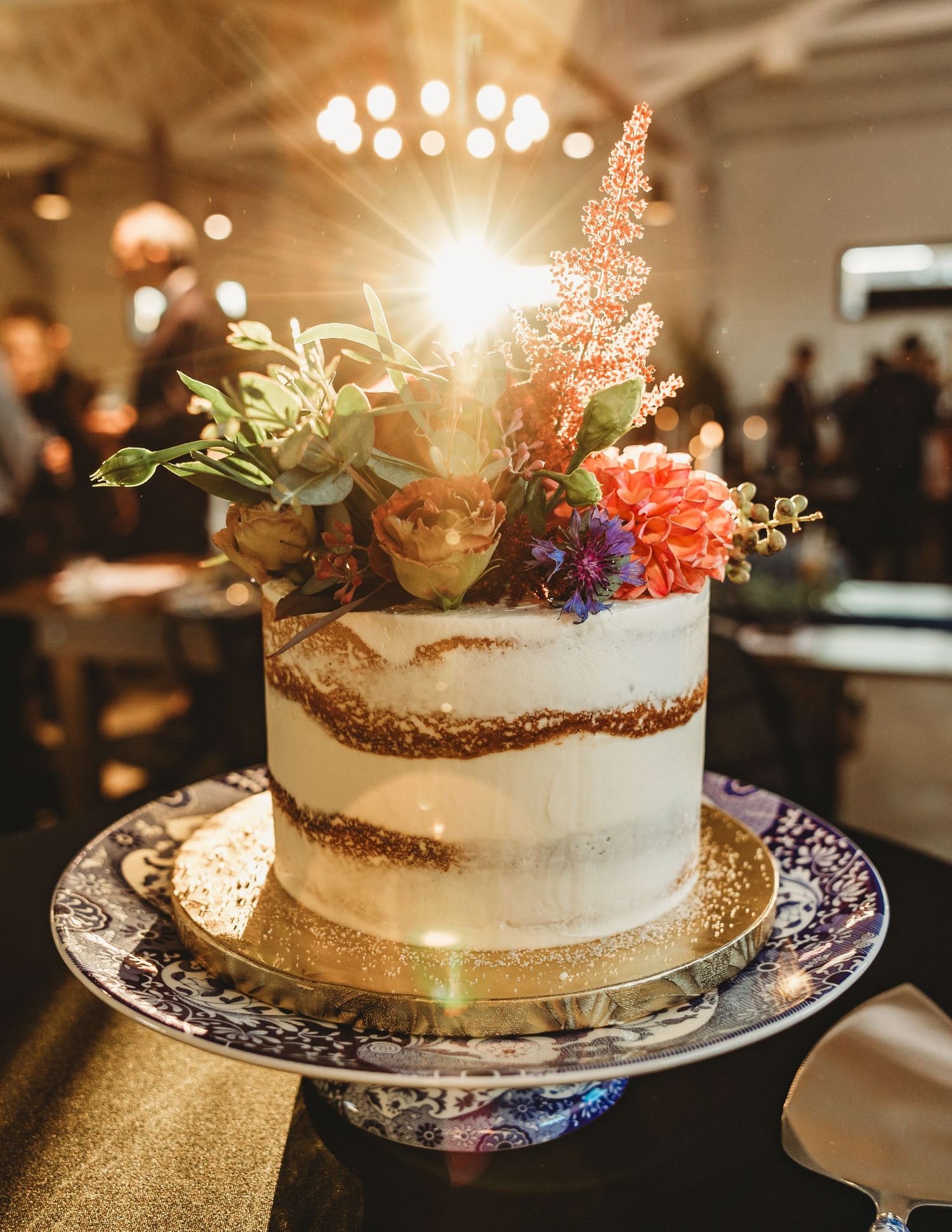 Semi-naked wedding cake decorated with fresh flowers on a vintage plate with golden accents.