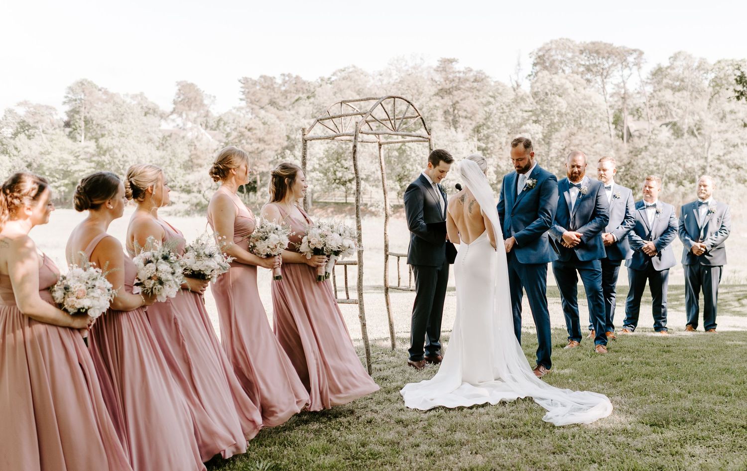 Wedding party and guests gather for an outdoor ceremony with pink and navy color scheme.