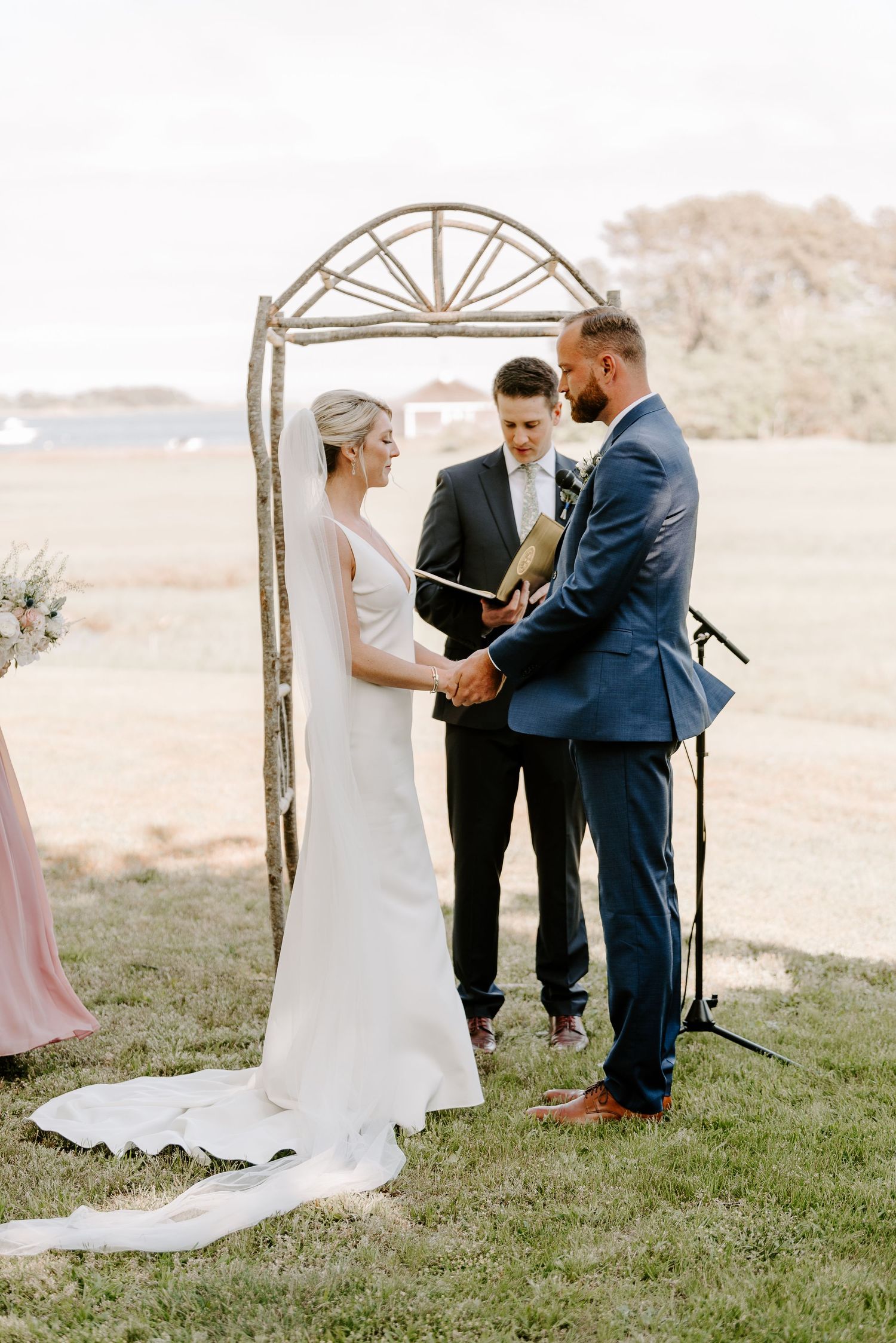 An intimate wedding ceremony unfolds beneath a handcrafted wooden arch at sunset.