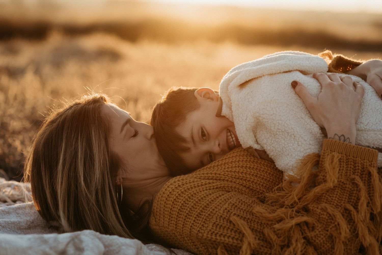 a mom kisses her sons head while he lays on her chest in a field at sunset in nampa idaho