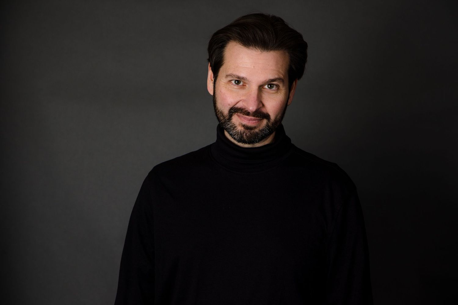 Dramatic studio portrait of a person in a black turtleneck against a dark background.