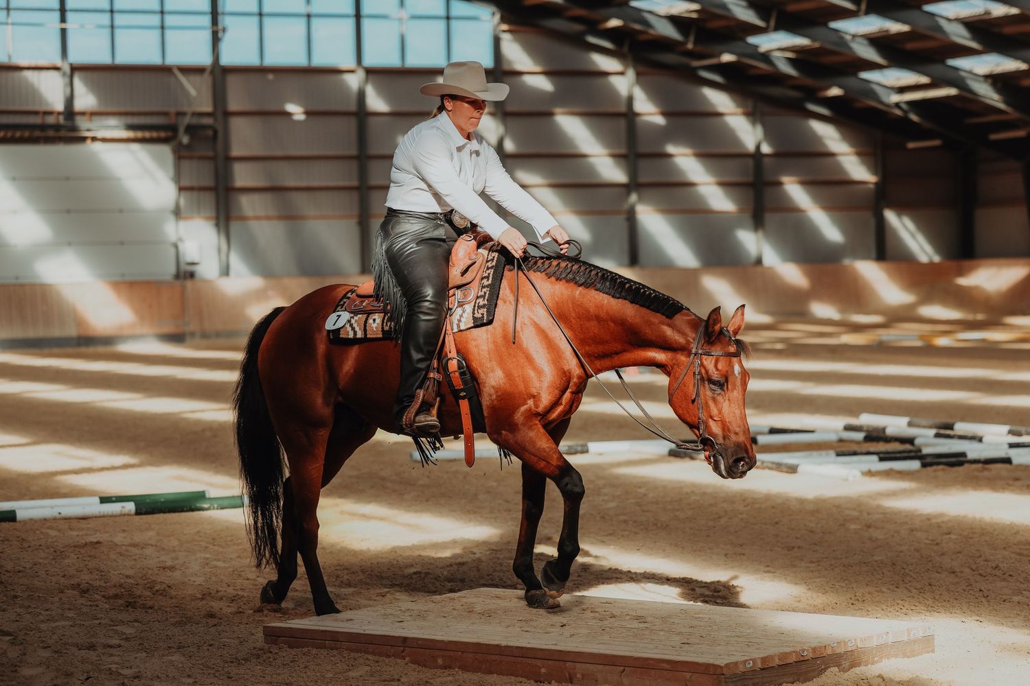 Western rider guiding a chestnut quarter horse through pole obstacles in an indoor arena.