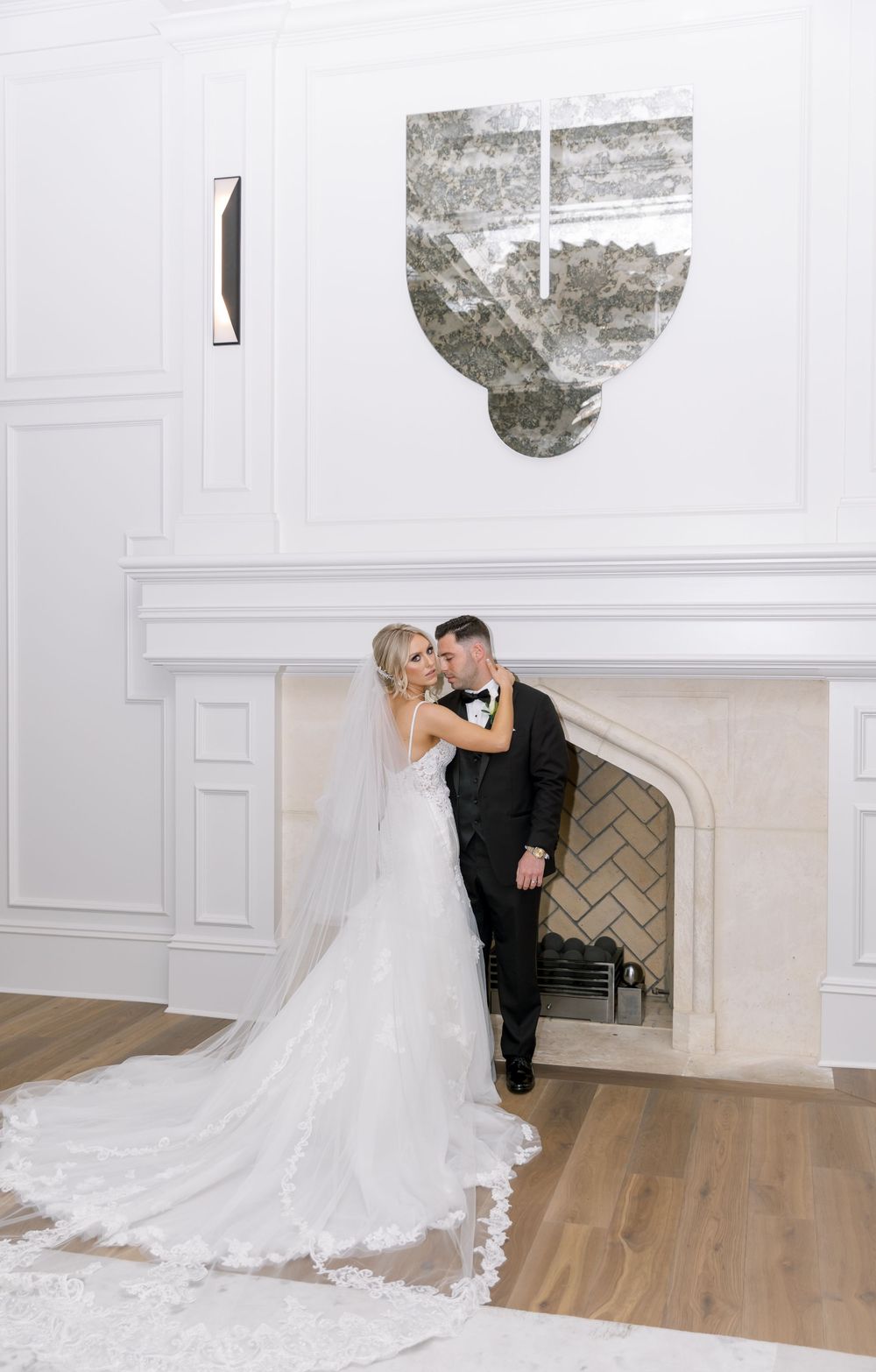 Wedding couple embracing near white fireplace with elegant decor.