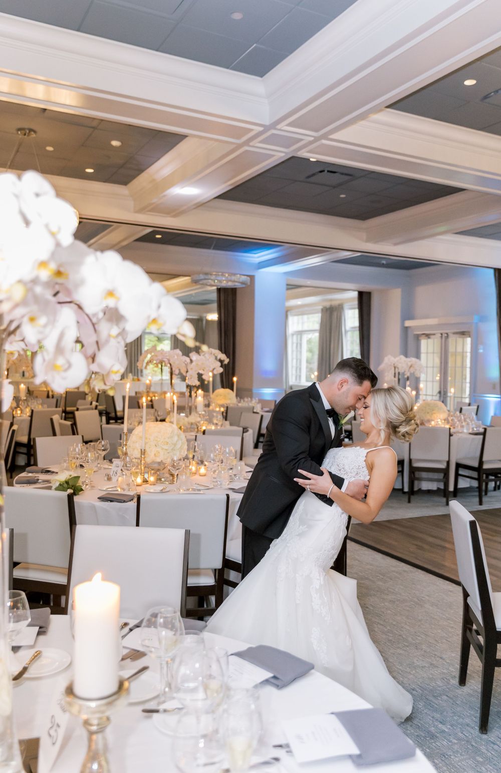 Romantic dance moment in elegant reception hall with orchid centerpieces and candlelight.
