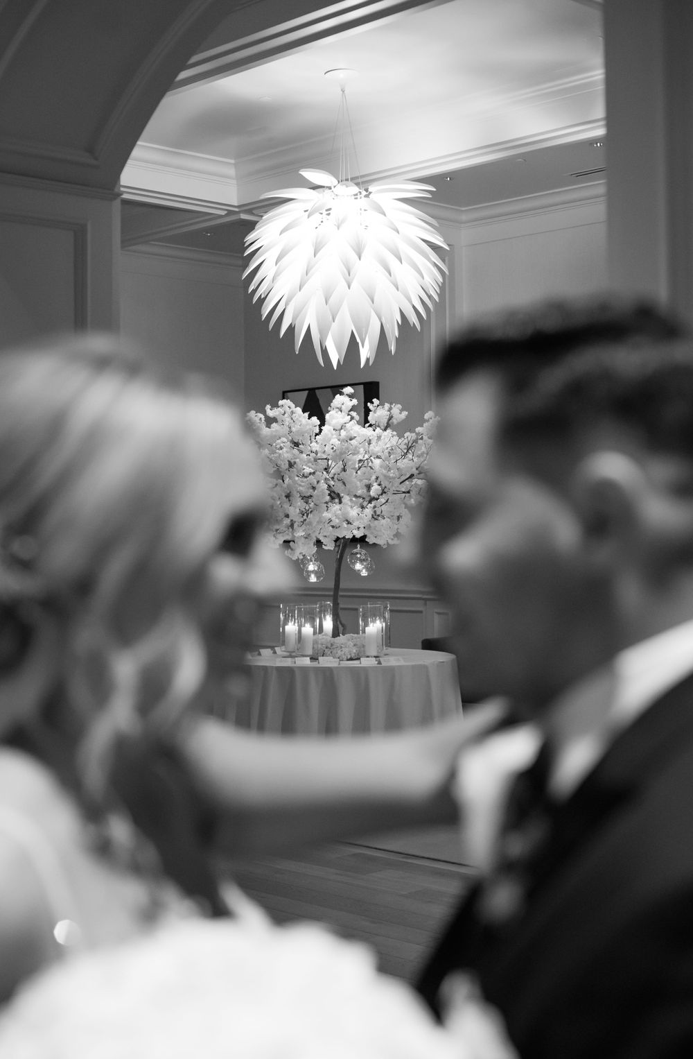 Black and white wedding reception detail with elegant white floral centerpiece and modern spiked chandelier.