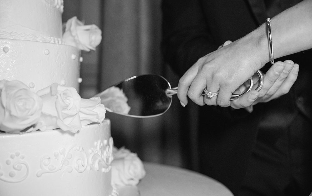 Black and white detail shot of cutting the white wedding cake.