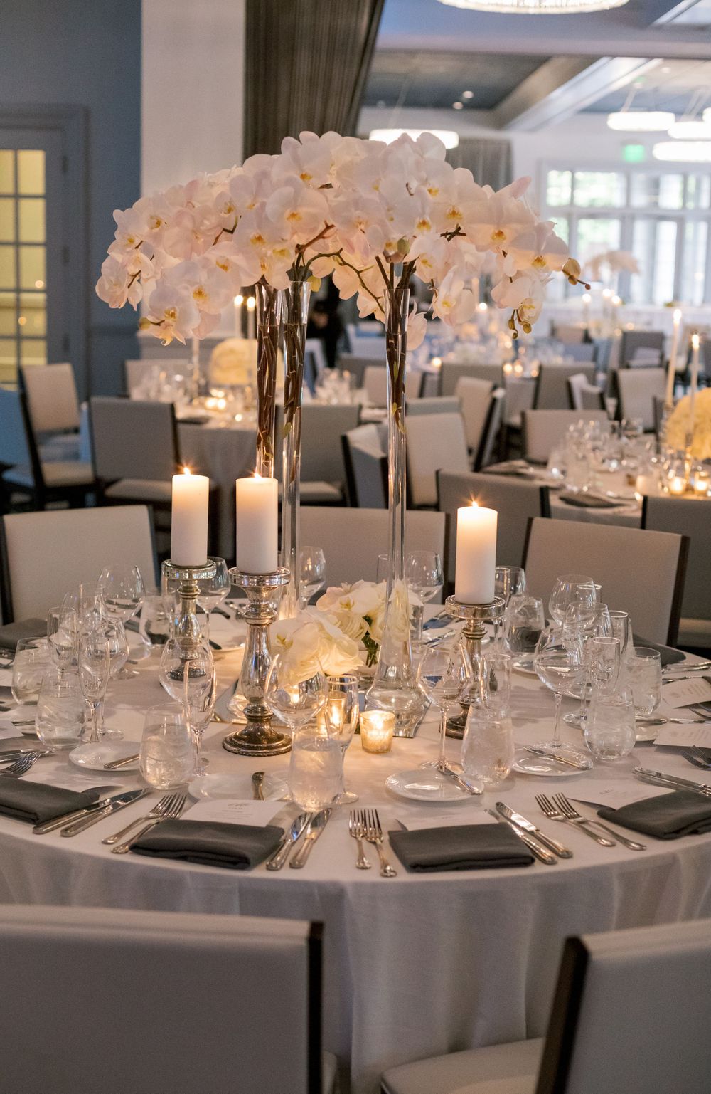 Luxurious wedding reception table with white orchid centerpiece, candles, and formal place settings.