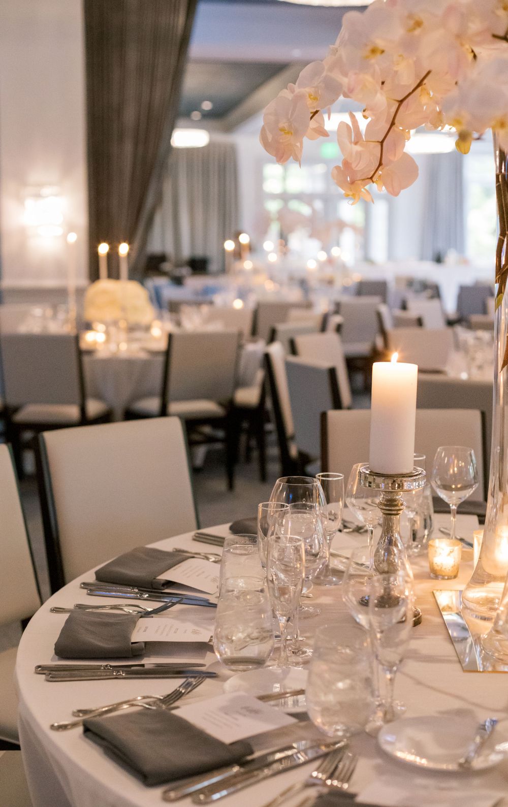 Elegant wedding reception table setting with white orchid centerpieces and candles in a modern banquet hall.