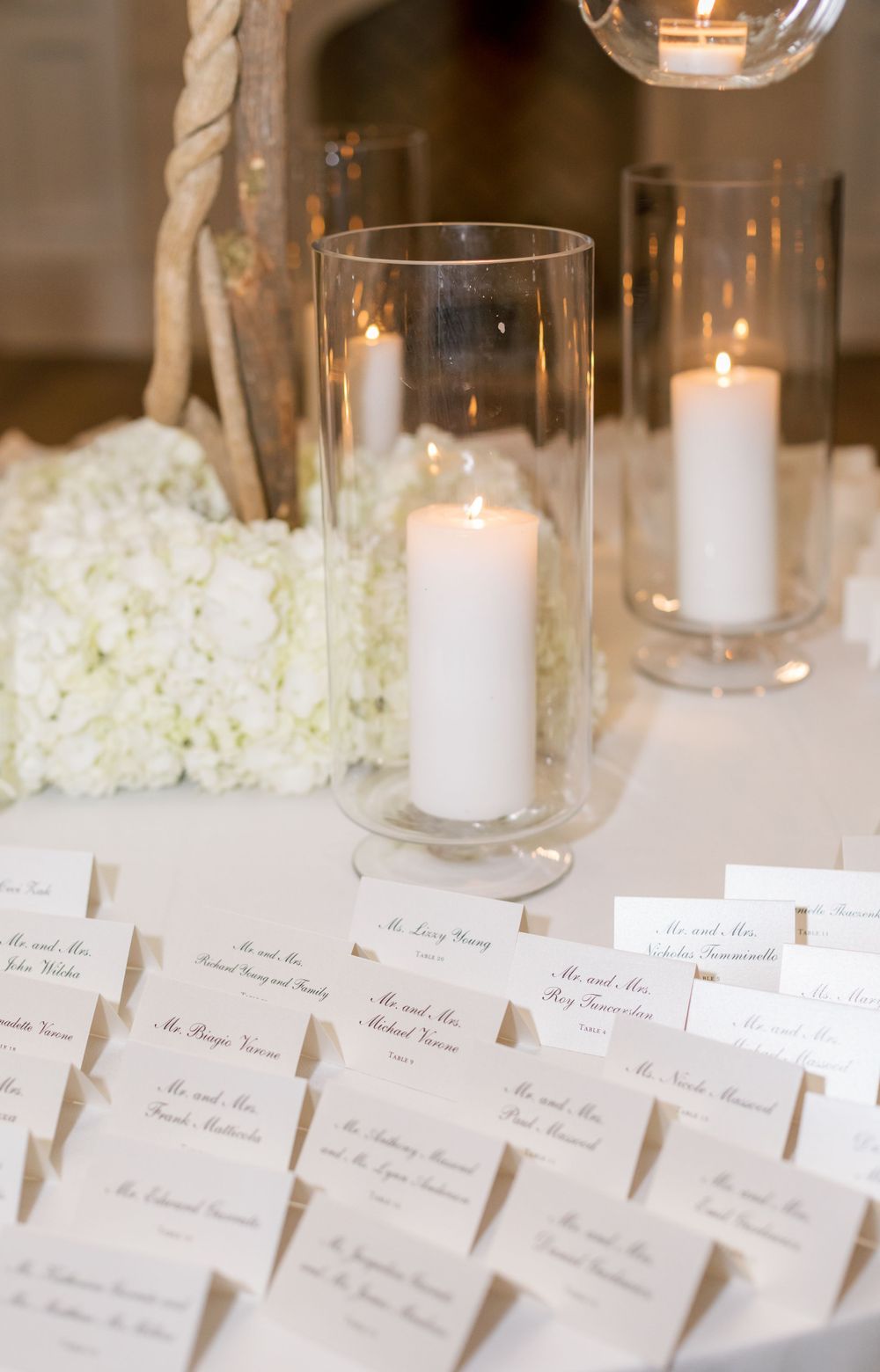 Elegant wedding reception place cards displayed with white pillar candles in glass holders.