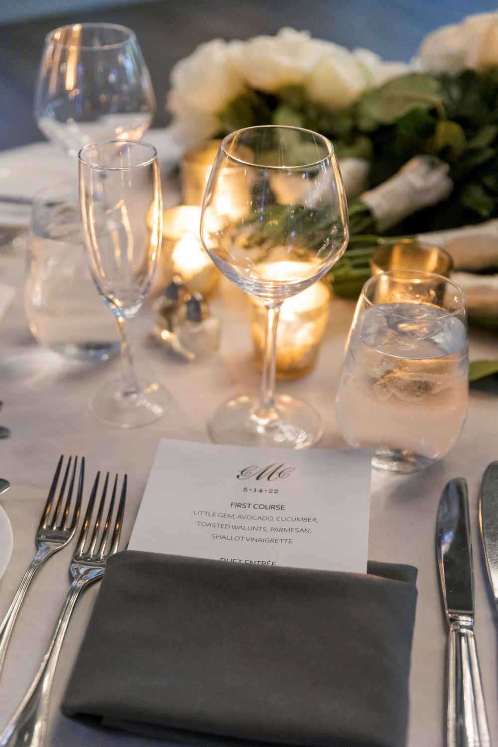 Close-up of formal place setting with wine glasses, menu card, and gray napkin at wedding reception.
