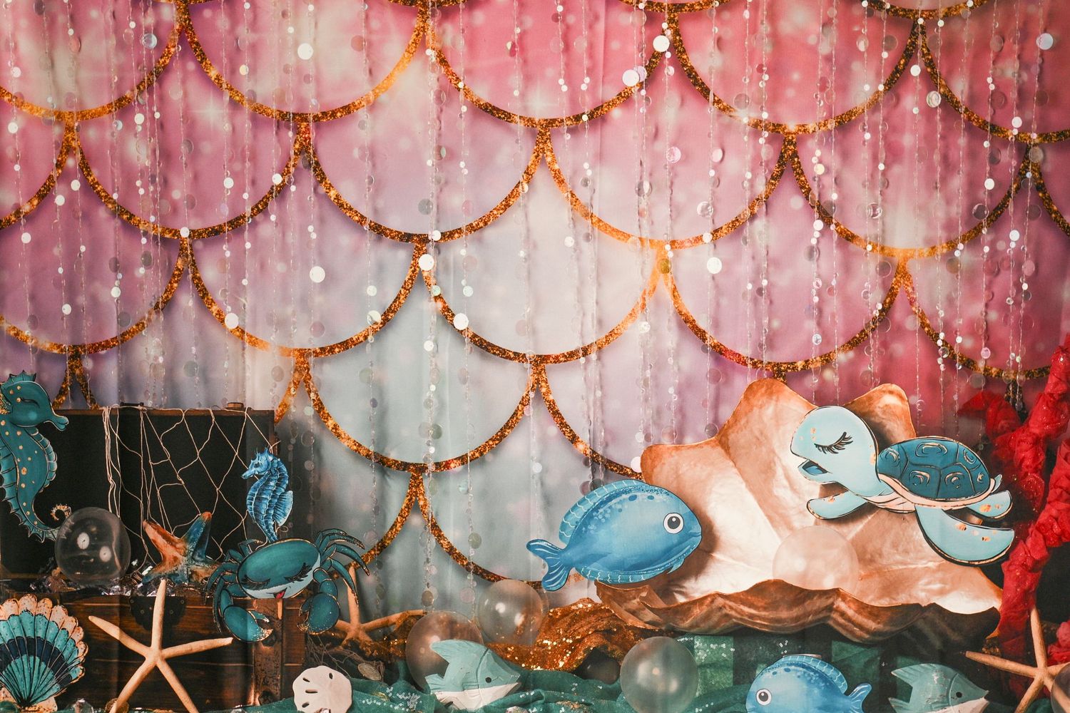Pink and gold mermaid-themed backdrop with scalloped pattern and twinkling lights.