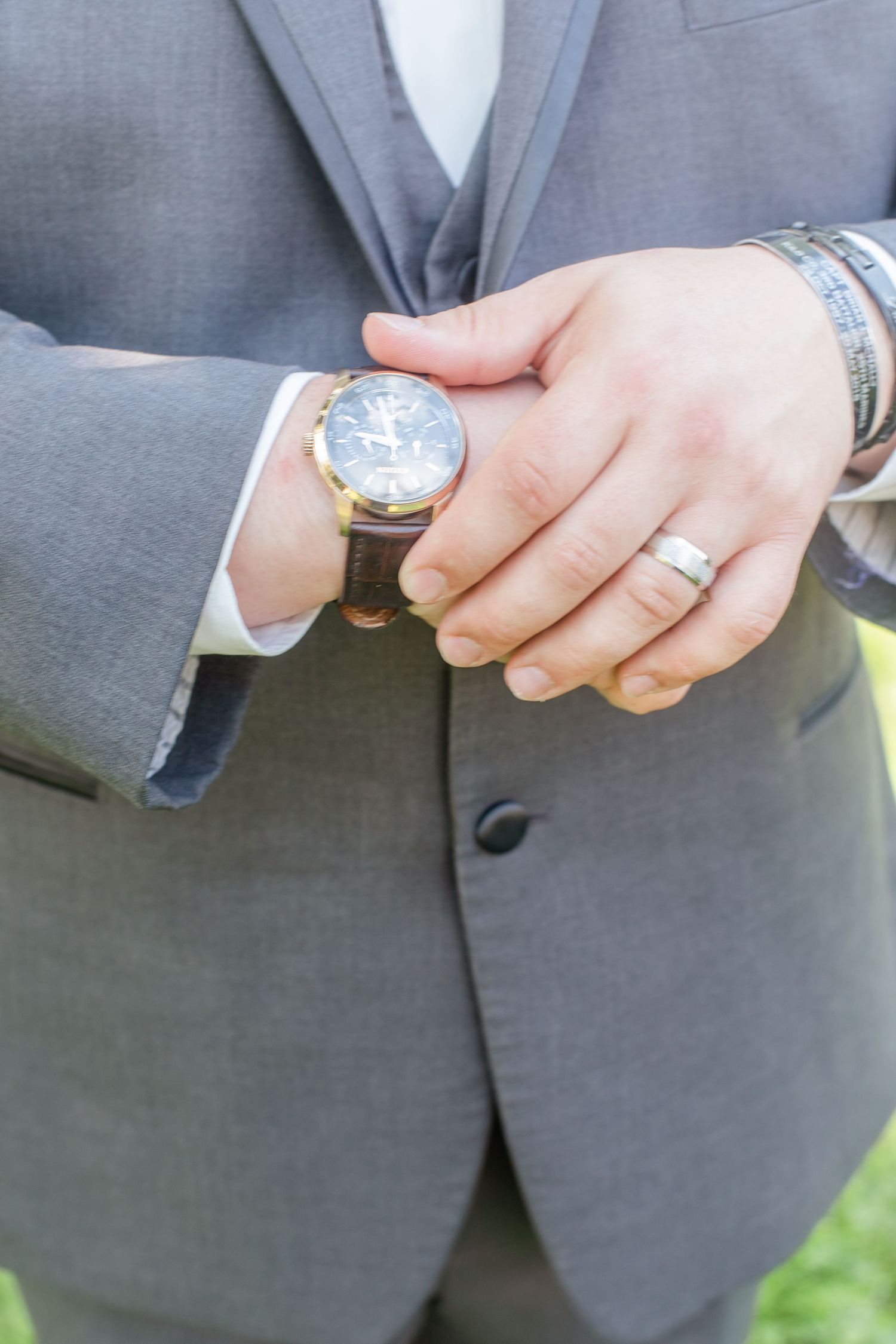 Close-up details of wedding rings and hands against grey suit fabric.