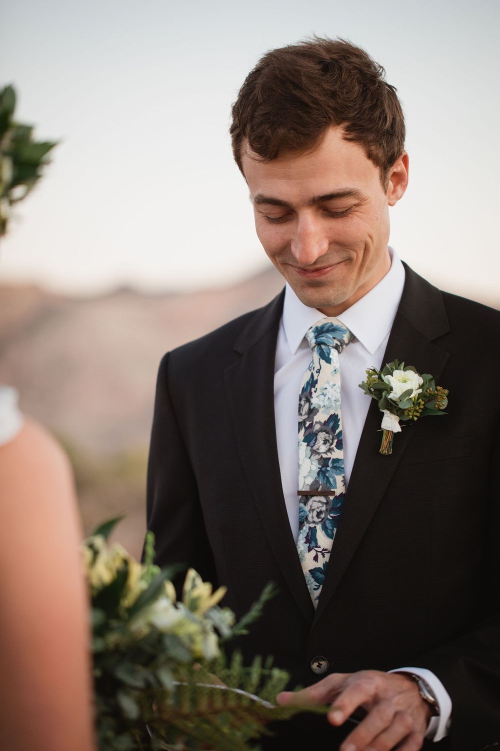 Groom smiles softly while reading wedding vows during an intimate outdoor desert elopement ceremony at sunset.