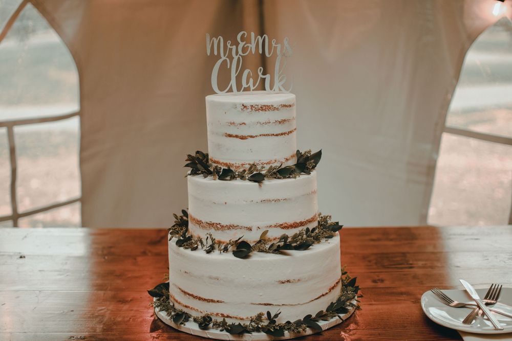 Three-tier naked wedding cake with greenery and a Mr & Mrs Clark cake topper.