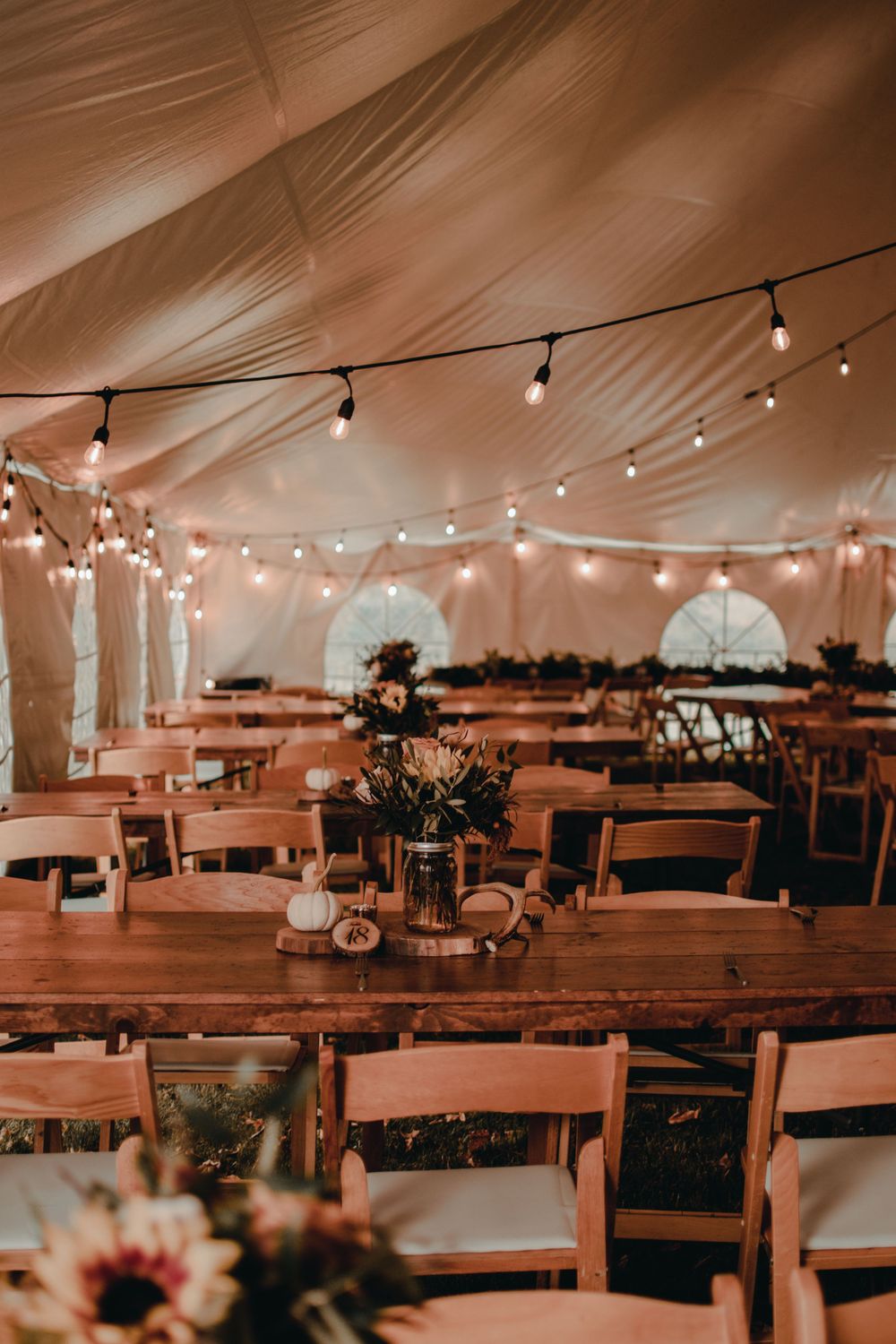 Elegant tent reception with string lights, wooden farm tables, and floral centerpieces.
