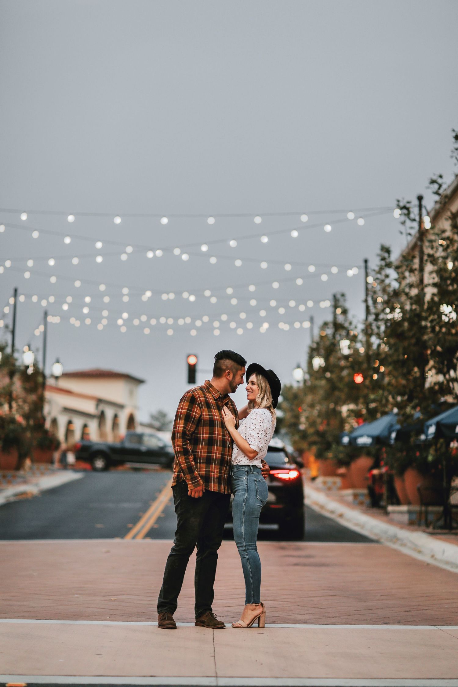 A romantic couple embraces under string lights on a quiet street at dusk in a charming downtown setting.