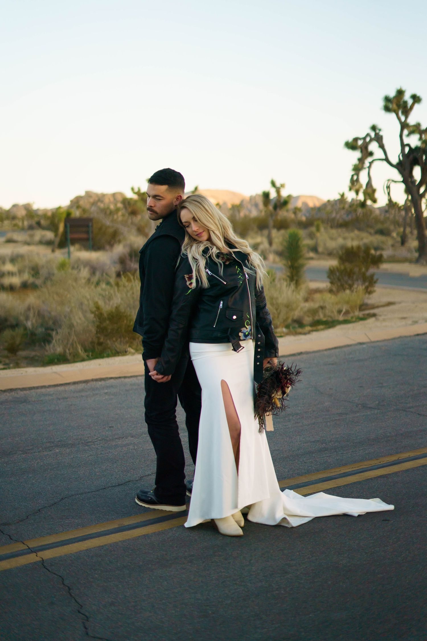 a bride and groom pose back to back in front of a motor cycle in Joshua tree National park