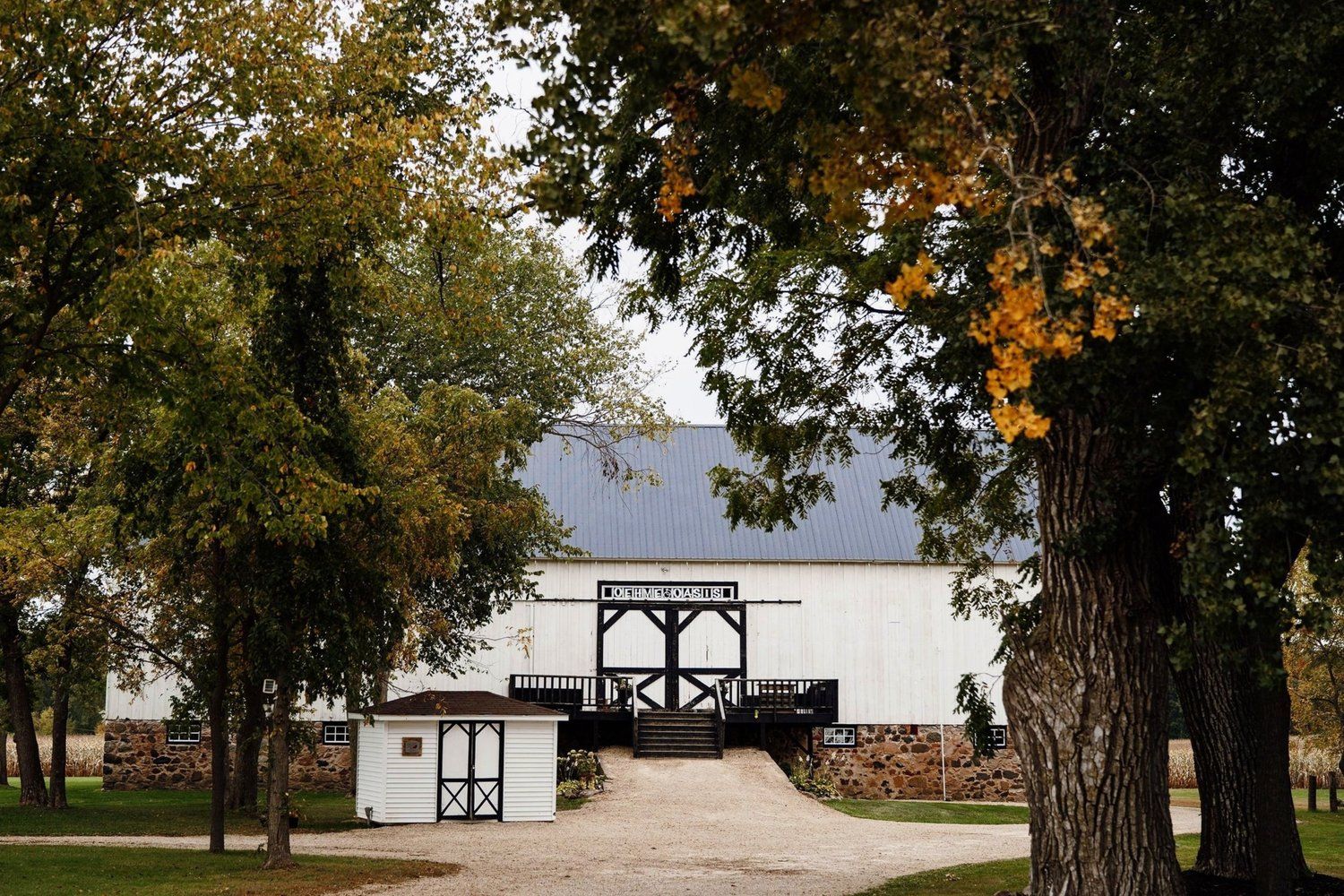 A white barn-style wedding venue with gothic windows framed by autumn trees.
