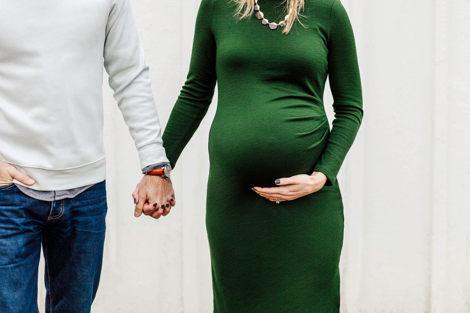 Couple holding hands with woman in green maternity dress showing baby bump.