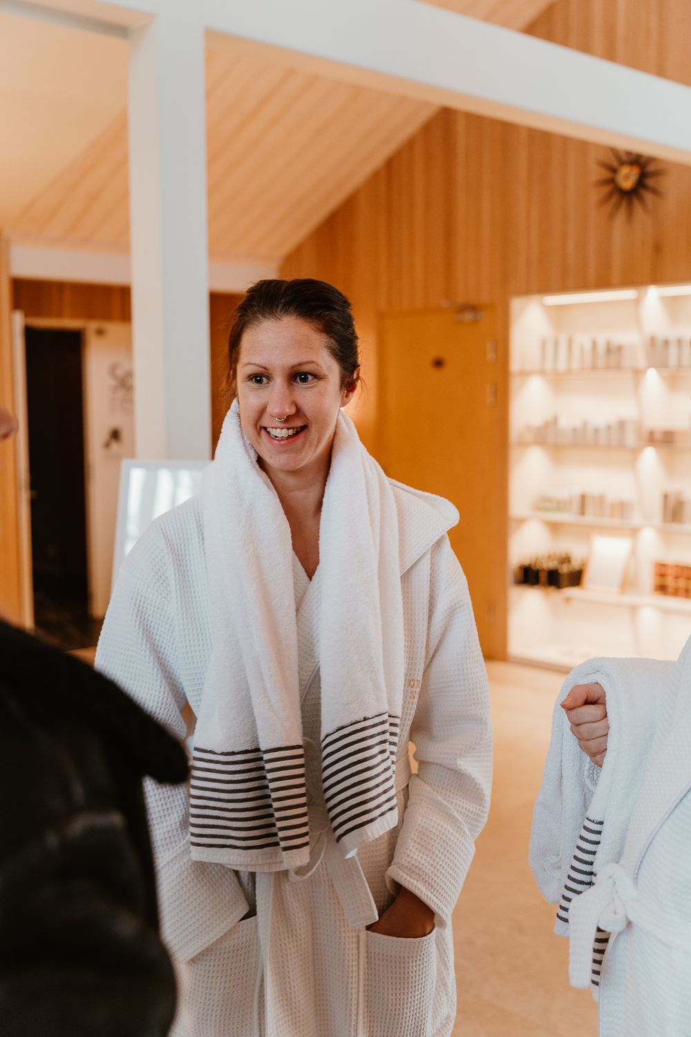 Person wearing white bathrobe with striped trim in warm-lit indoor space.