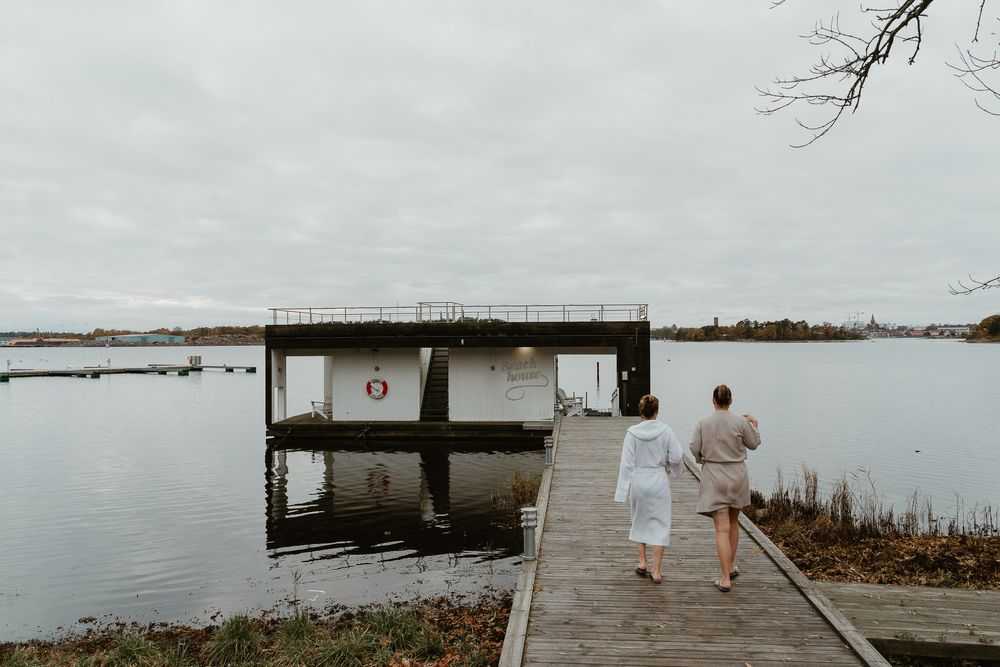 Two people walking down wooden dock towards water on overcast day.