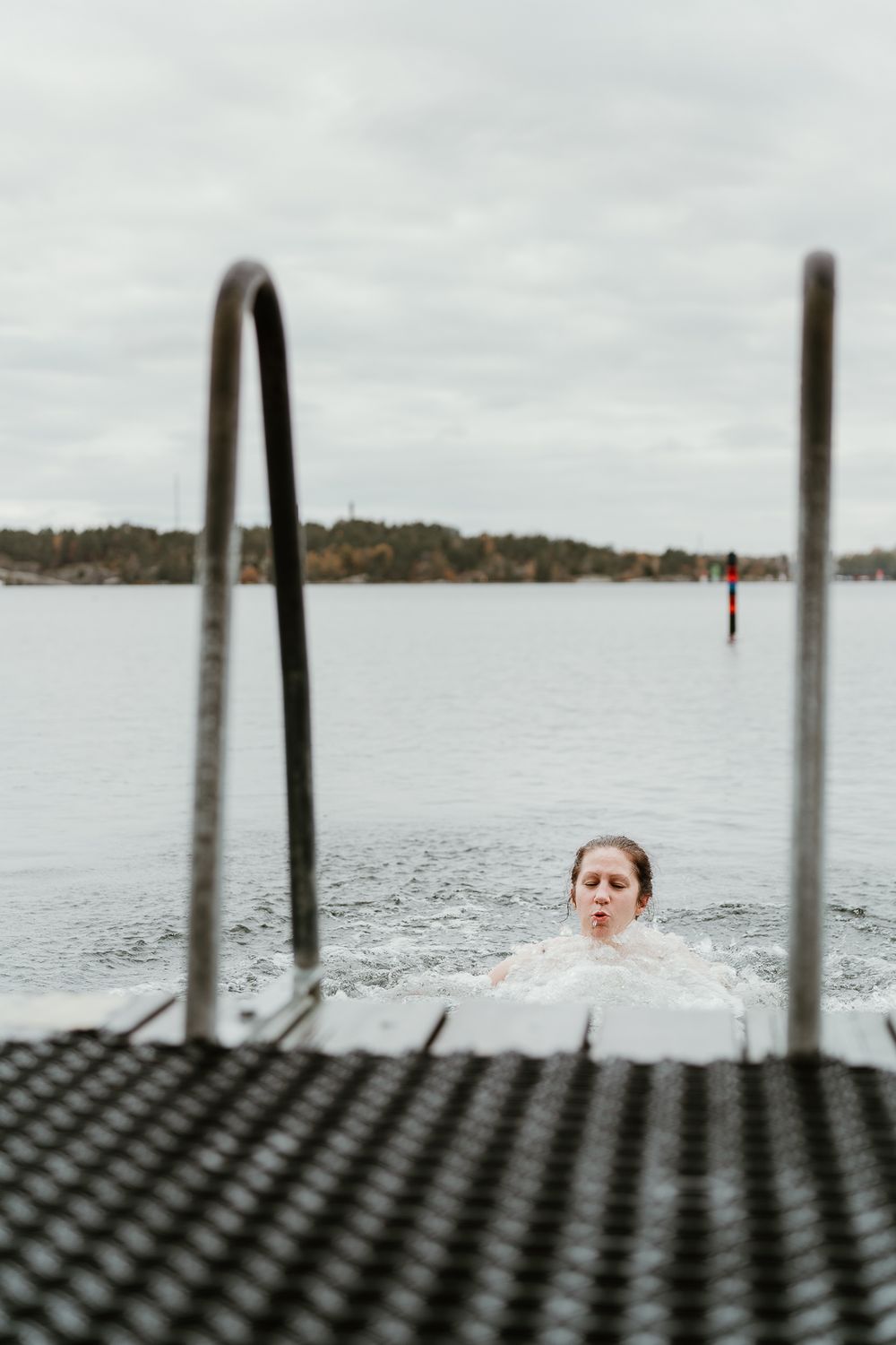 View through metal railings of someone swimming in a calm lake on a cloudy day.