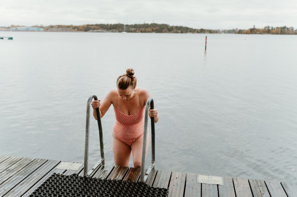 A swimmer emerges from the water using metal handrails on a wooden dock.
