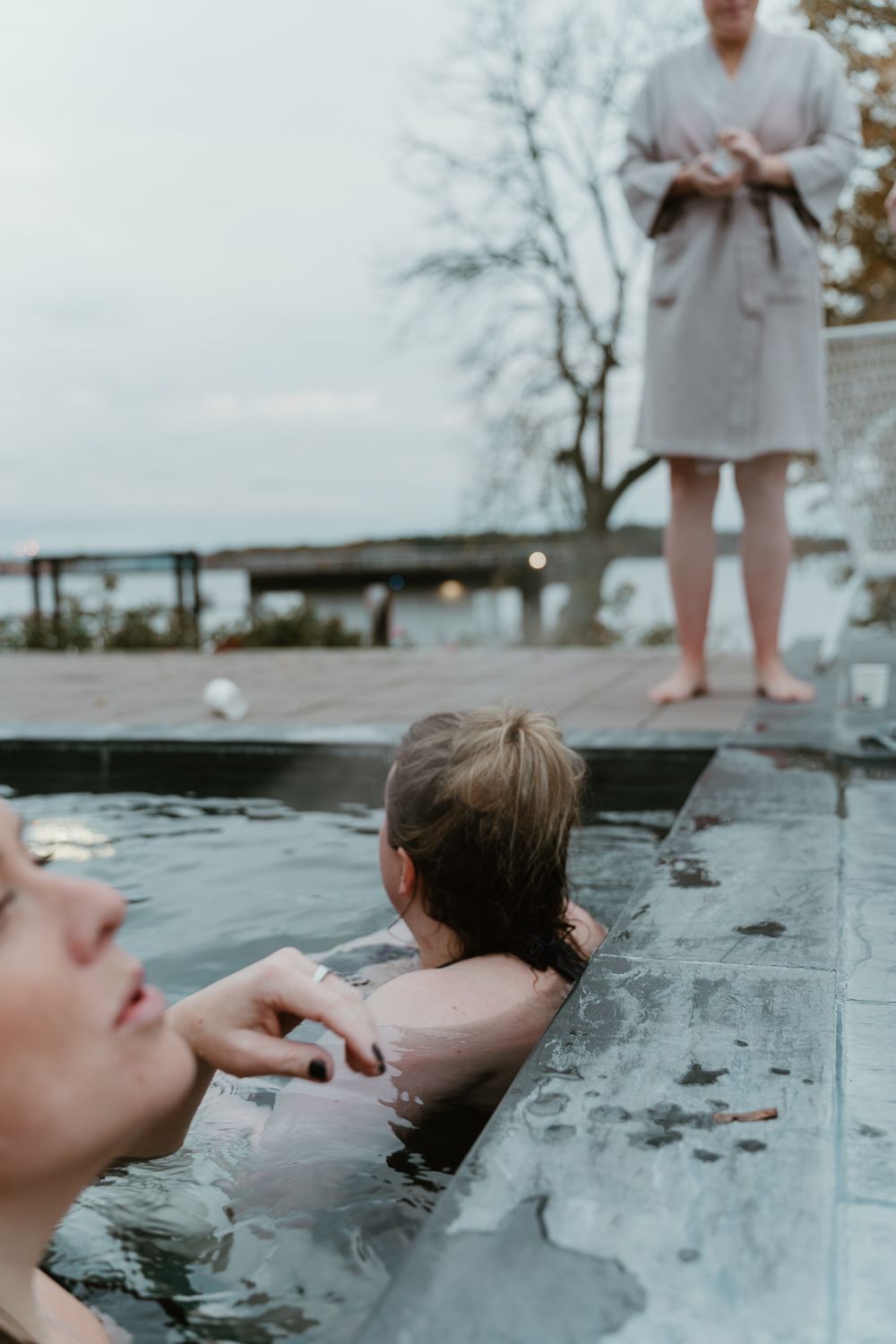 People relaxing in a heated outdoor pool with lake and trees visible in background.