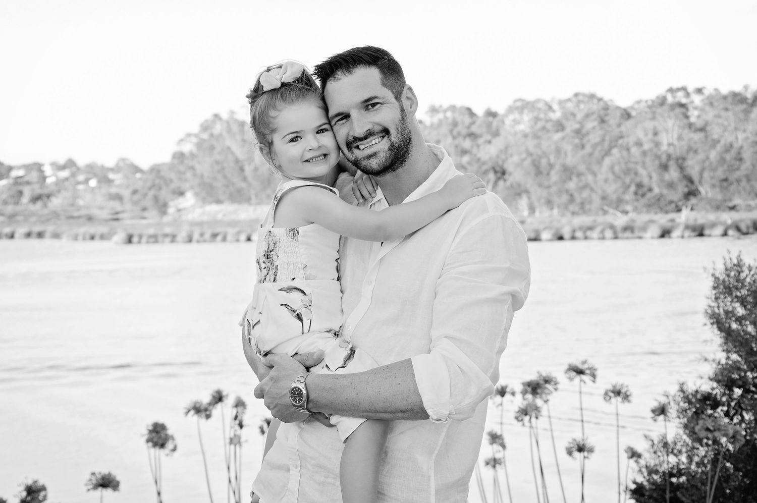 father holding young daughter smiling at camera outside