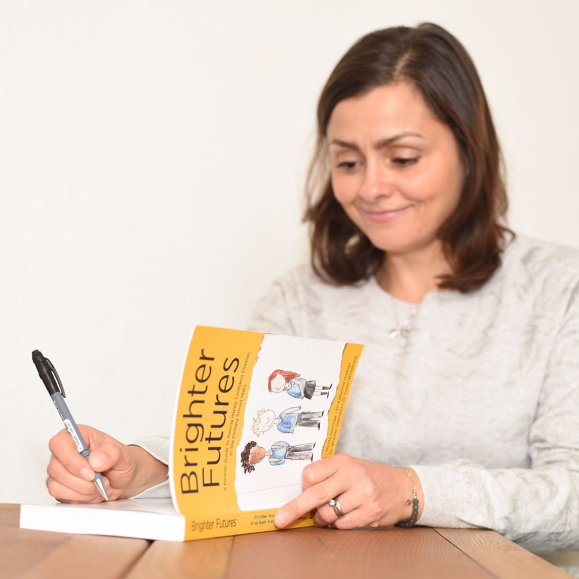 Dr. Lucy Russell, seated at a table, signs her book "They Are the Future" during a branding photo shoot by Abigail's Studio.